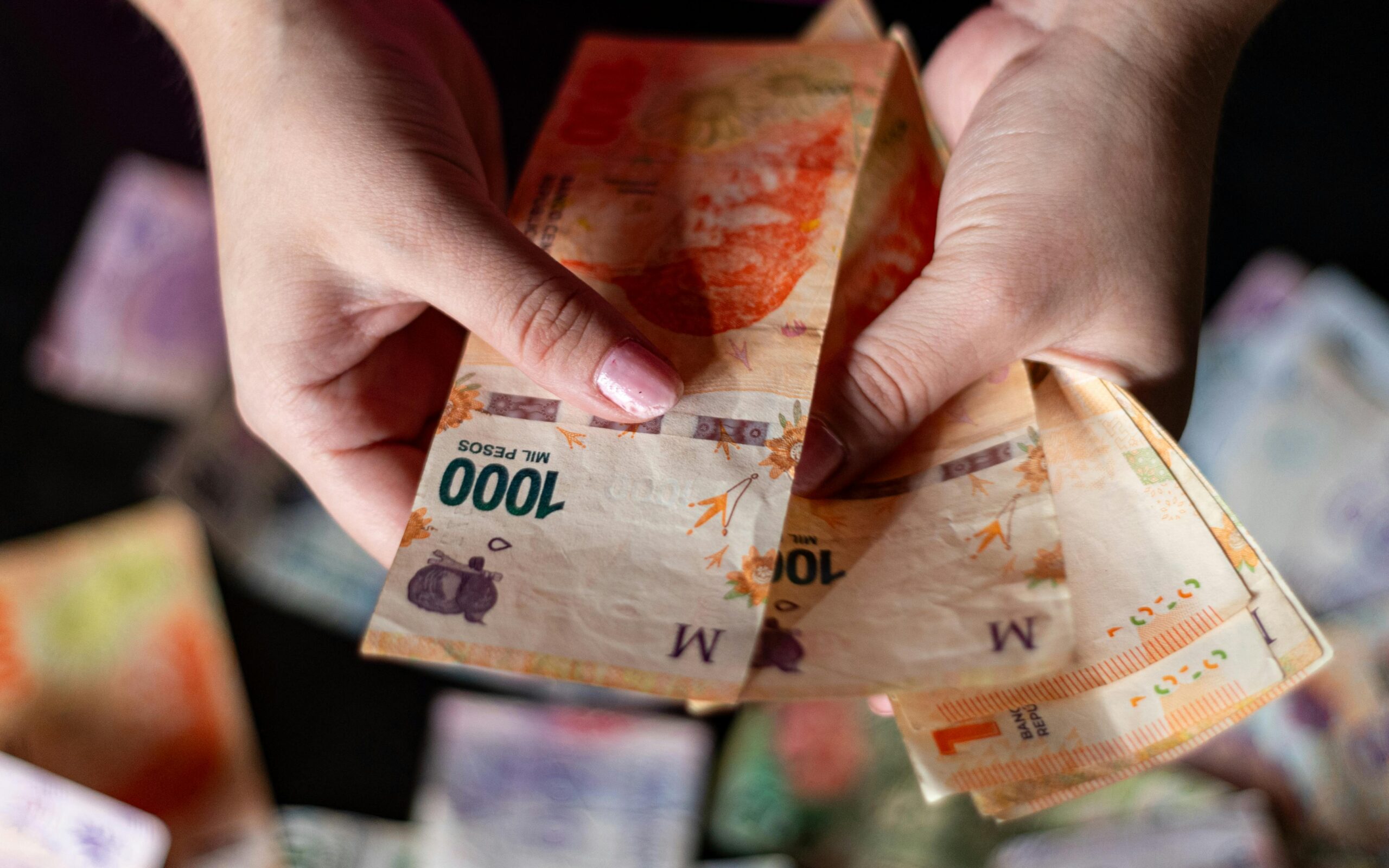 Hands holding Argentine peso banknotes, showcasing currency details in Buenos Aires.